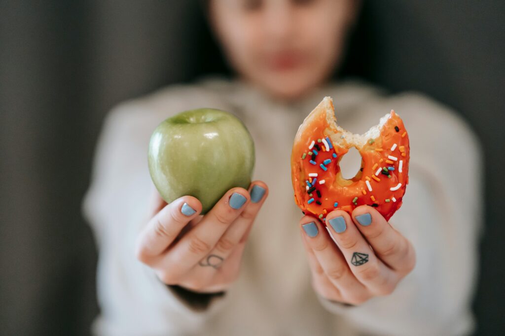 Two hands: one holding an apple, one holding a doughnut with a bite out of it.