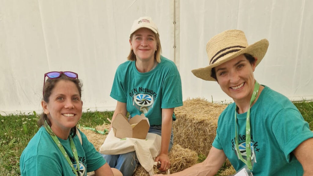 AFN Champions Amy Jackson, Charlotte Wheeler and Georgie Barber smiling, sitting on hay bales in the AFN tent