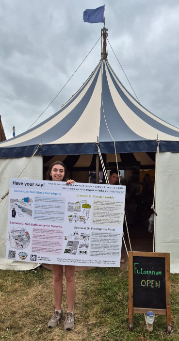 A woman holds up a poster in front of a tent.