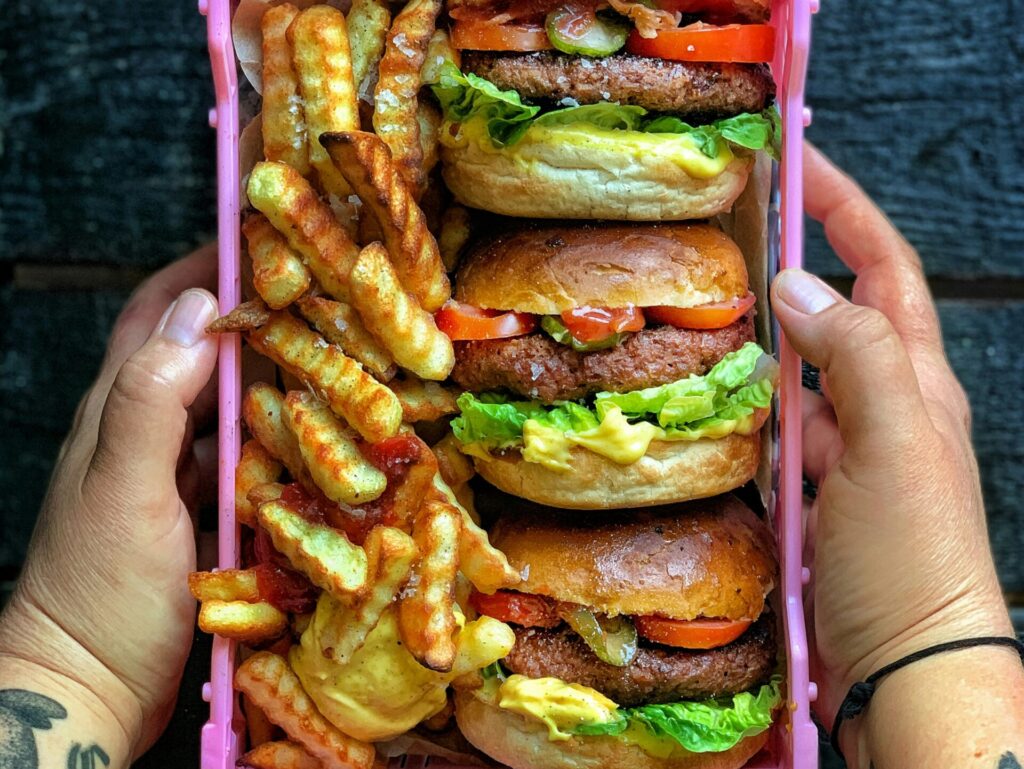 Two hands holding a tray of burgers and chips.