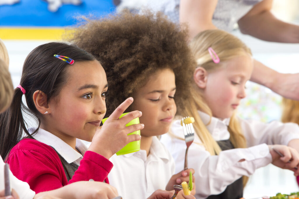 primary school pupils sit at a table eating their school lunch